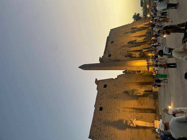 Luxor Temple glows with floodlights at dusk around a towering obelisk and seated statues.