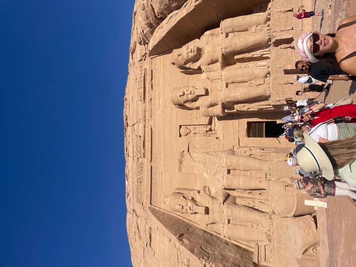Crowds gather at the colossal statues and entrance of Abu Simbel carved into a sandstone cliff.