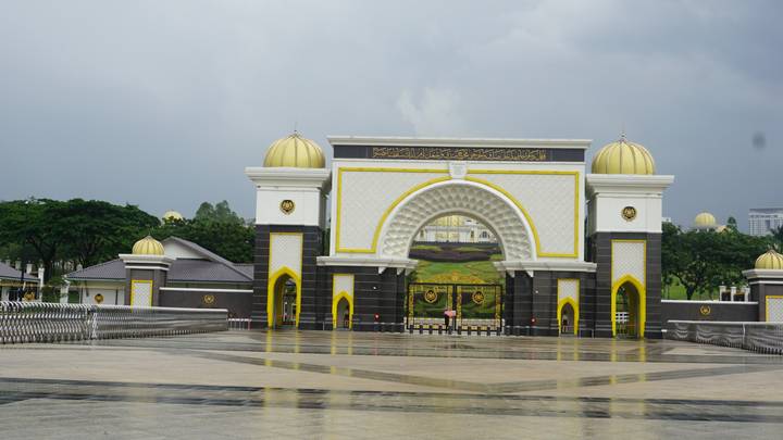 The ornate golden-domed gate of Malaysia’s National Palace reflects on wet marble after rain.