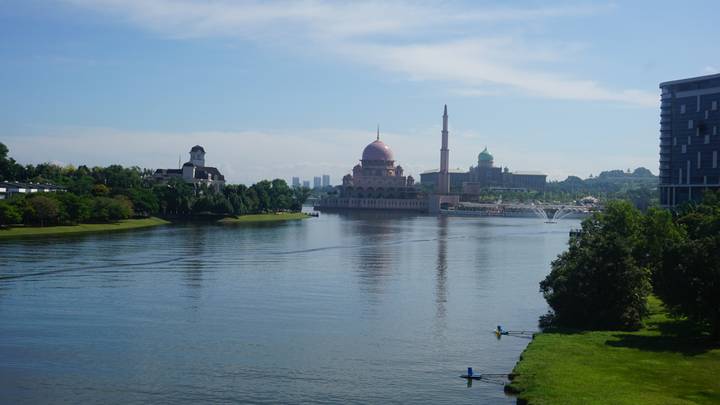 The pink-domed Putra Mosque sits beside a calm lake under clear blue skies.