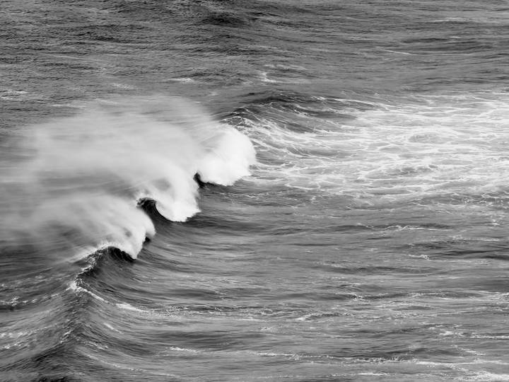 Black-and-white capture of powerful ocean waves breaking and spraying mist.