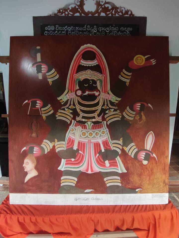 Traditional Sri Lankan mural depicting a multi-armed deity on a red background inside a temple.
