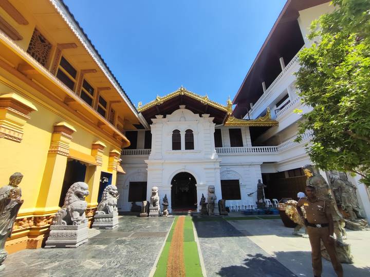 Courtyard of an ornate white and gold Buddhist temple guarded by stone lions under a bright blue sky.