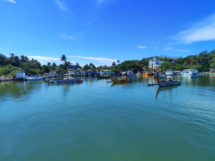 Calm harbour with colourful fishing boats reflected in turquoise water under a bright sky.