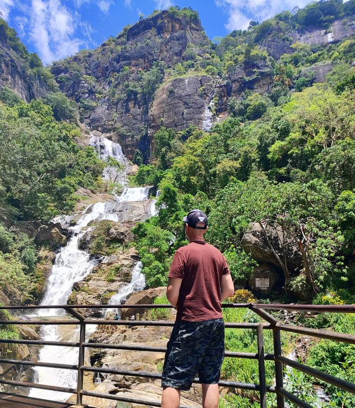 Traveler observing a multi-tiered jungle waterfall cascading down rocky cliffs.