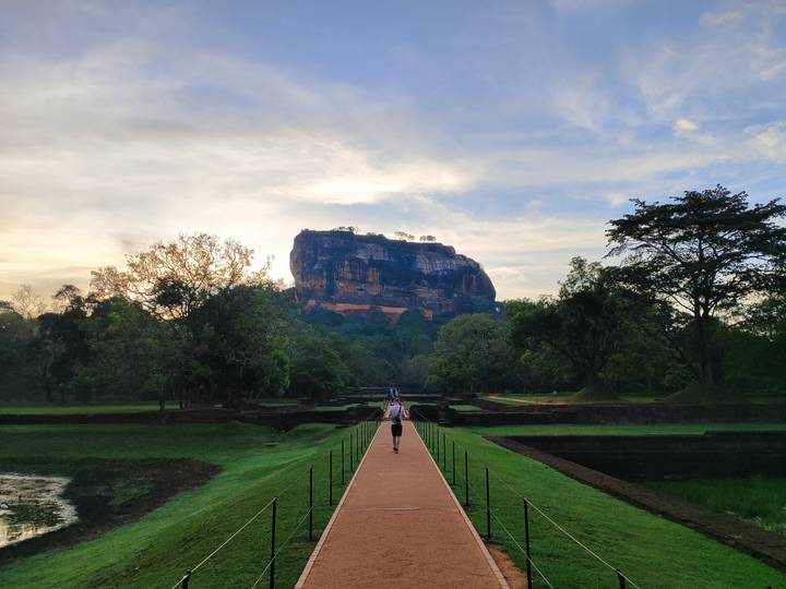 Traveler walking the long brick path toward the iconic Sigiriya Rock fortress at sunrise light.
