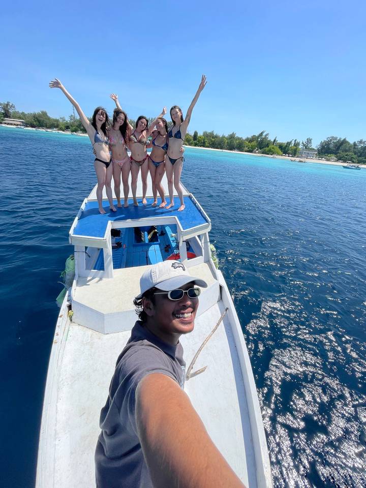 Selfie of a guide on a boat with five women standing on the roof against turquoise island waters