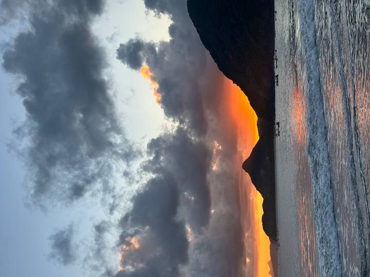Dramatic sunset with orange glow behind mountainous coastline and gentle surf