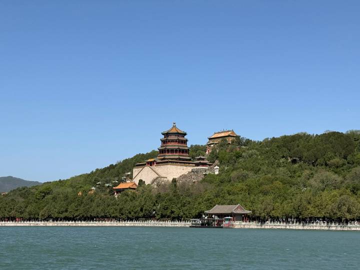 The Tower of Buddhist Incense rises above lush trees on Longevity Hill, reflected in the still waters of Kunming Lake beneath a cloudless blue sky.