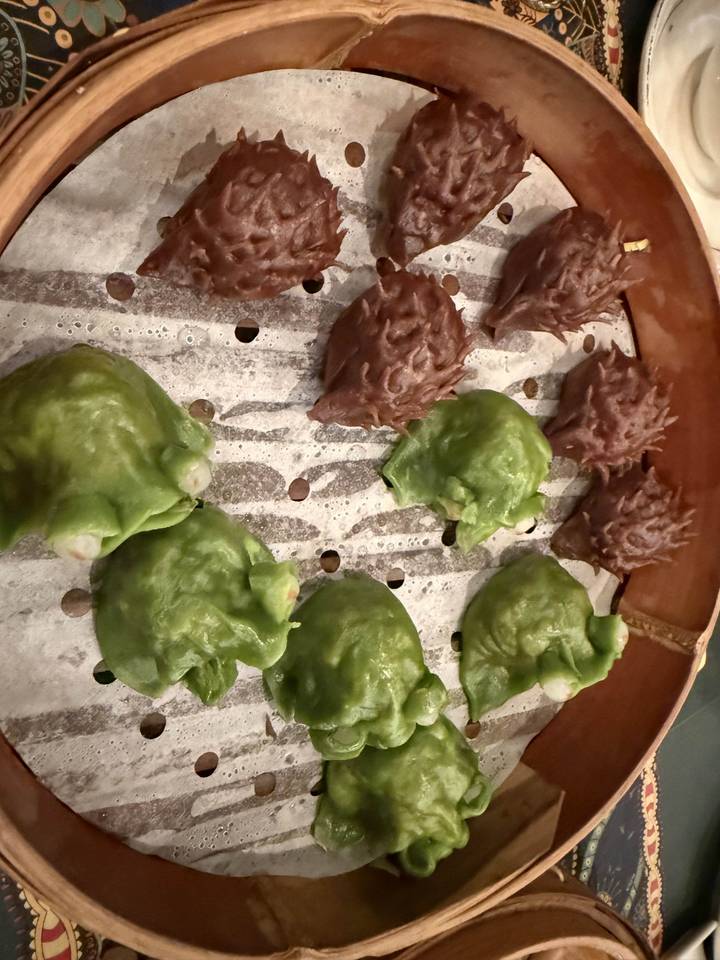 Close-up of steamed green and brown dumplings with textured wrappers arranged on a perforated tray inside a bamboo steamer.