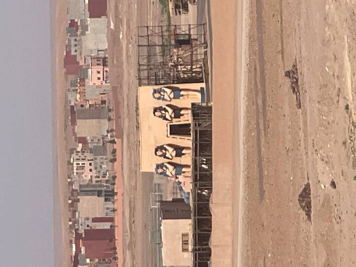 Distant view of an unfinished movie set with large Egyptian female statues in a desert edge town.