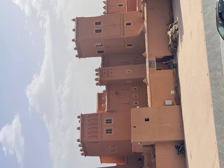 Adobe towers of a kasbah with a couple of locals near the entrance on a hazy afternoon.