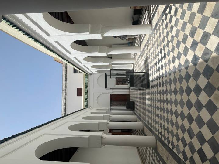 Bright interior courtyard with white arches, chequered floor tiles and display cases.