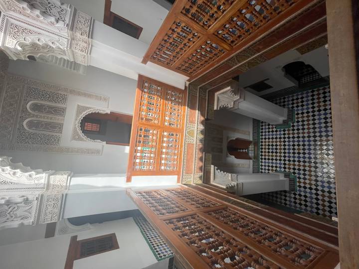 Multi-level interior of a traditional Moroccan riad featuring carved wood balconies and colourful zellige tiles.