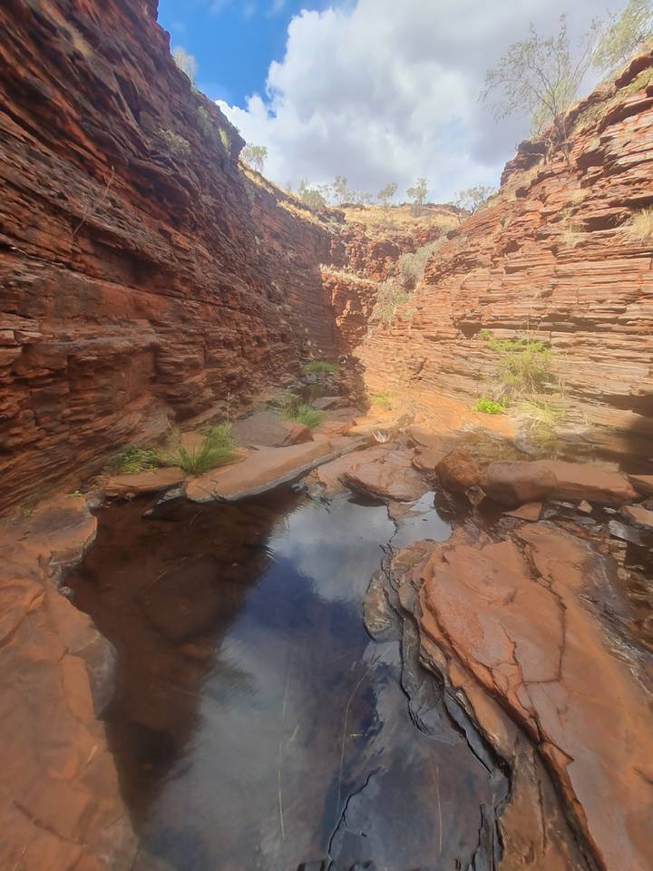 A rocky gorge with shallow pools reflects canyon walls under harsh midday light.