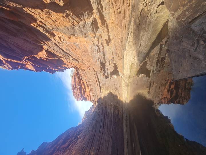A narrow red-rock gorge with still water reflecting towering sandstone walls under a clear blue sky.
