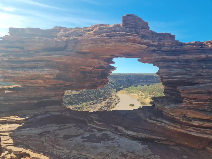 A natural sandstone window frames a river winding through a green gorge below.