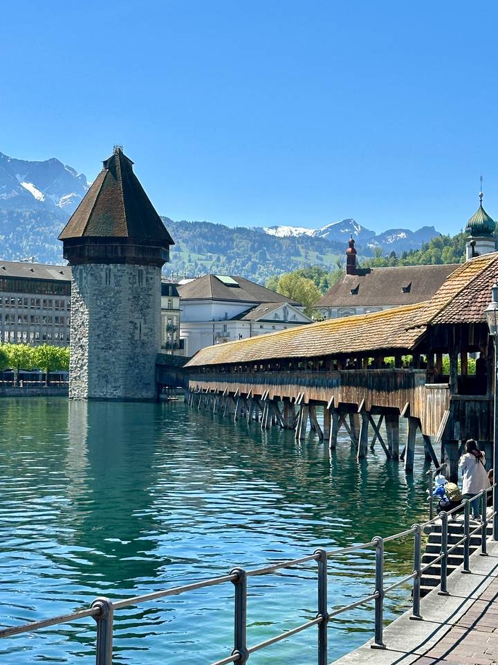 Lucerne’s wooden Chapel Bridge spans calm blue water with alpine peaks behind.