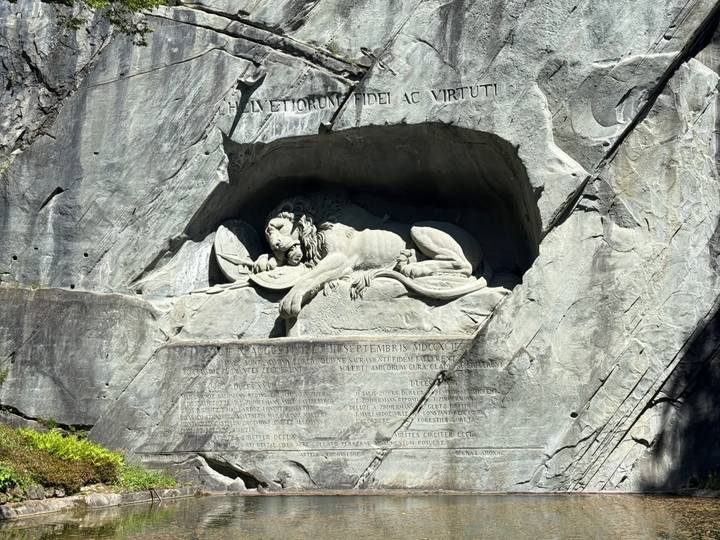 The Lion Monument in Lucerne carved into a sheer rock face illuminated by sunlight.