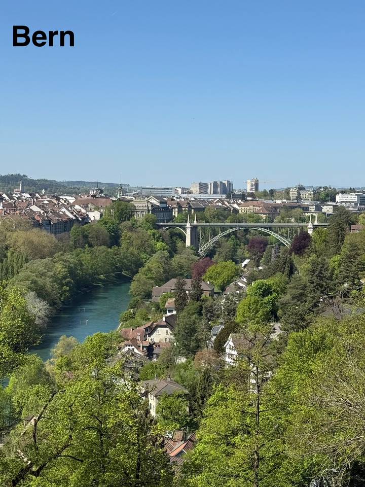 Panoramic view over Bern with the Aare river and a green valley framed by bridges.