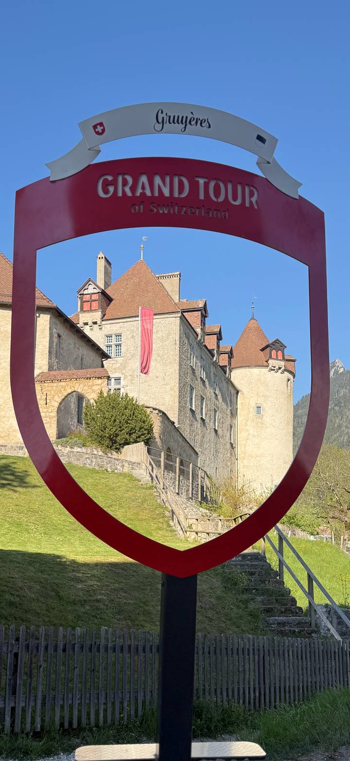 Medieval Gruyères Castle framed by a large red sculpture under blue skies.