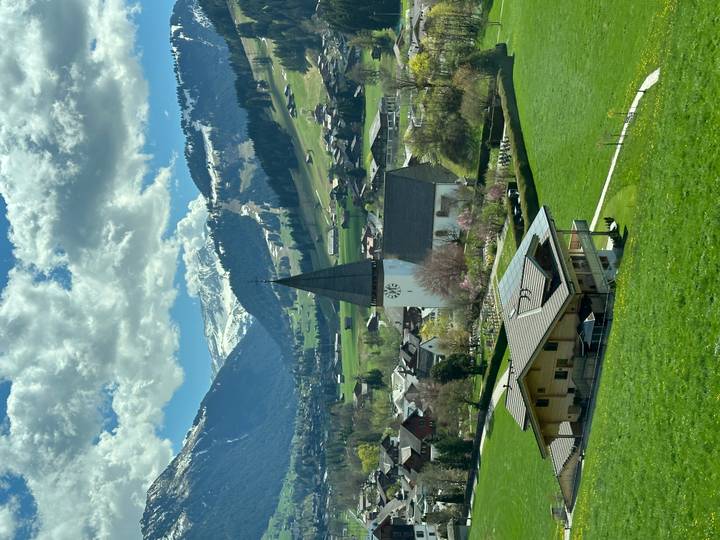 Picturesque alpine valley with a tall church steeple and snow-dusted peaks beyond.