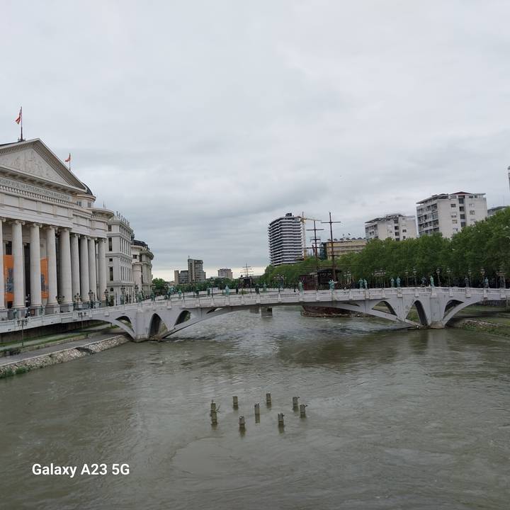 Elegant white pedestrian bridge and riverside museums in a modern Balkan city under cloudy skies.