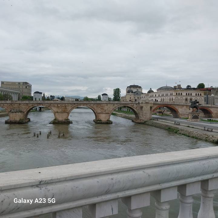Historic multi-arch stone bridge crossing a wide river with Ottoman-style buildings beyond.
