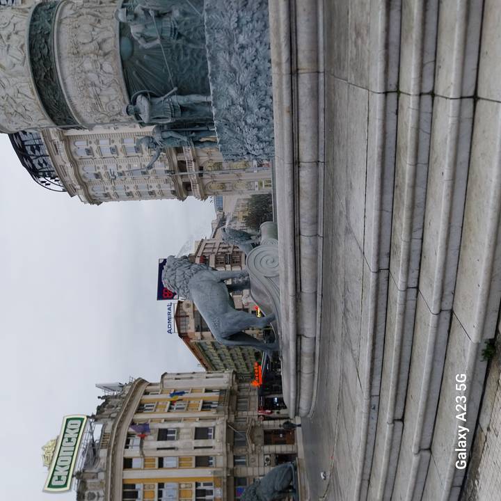 Marble plinth with bronze lion statue in a busy city square lined by ornate buildings.