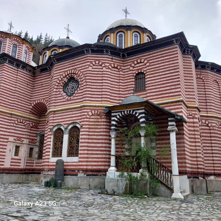 Striped red and white monastery walls with intricate windows and archways surrounded by mountains.