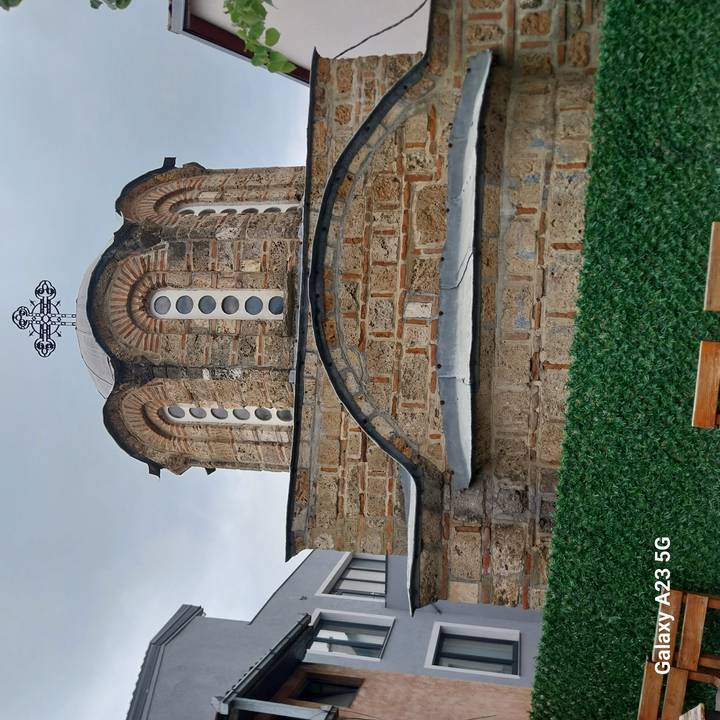 Small stone Orthodox chapel with circular windows and brick detailing beneath a cloudy sky.