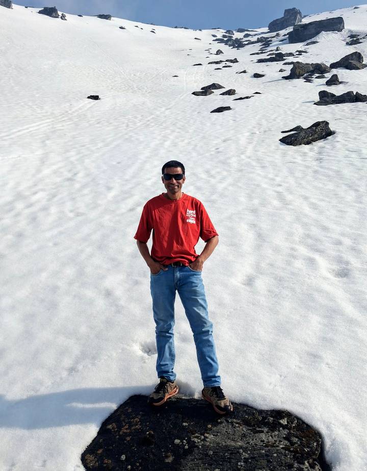 Smiling traveller in red shirt stands on a vast patch of untouched snow under bright light.