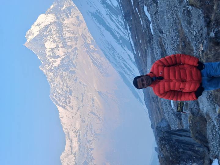 Portrait of hiker in orange jacket with dramatic snowy Himalayan backdrop in early morning light.
