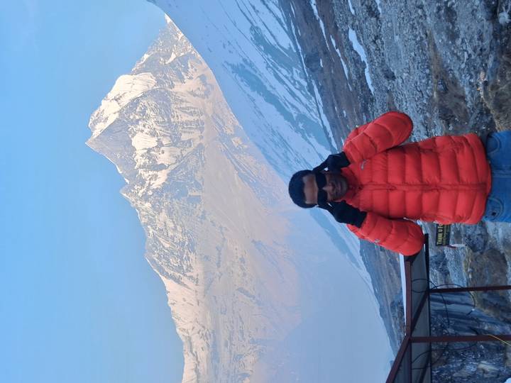 Hiker adjusting sunglasses while standing before a dramatic snow-capped Himalayan summit.