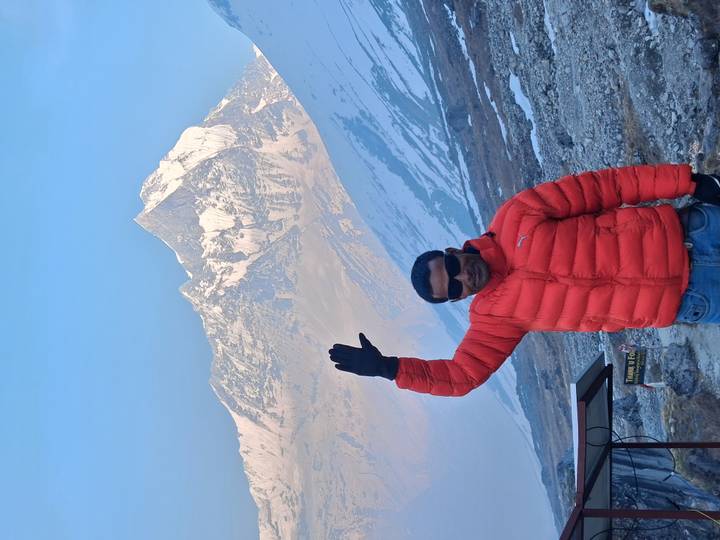 Smiling trekker waving with dramatic snowy mountain backdrop in Nepal.