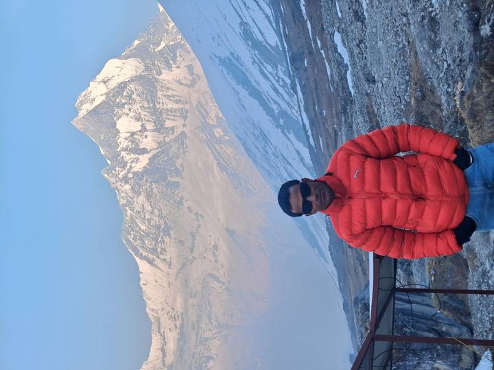 Portrait of a traveler in a puffy red coat set against the Himalayan range.