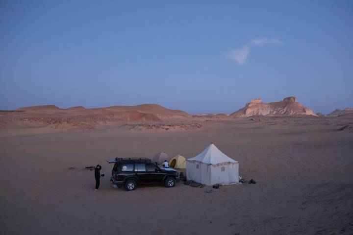 4x4 vehicle, canvas tents and solitary camper set up in vast desert at twilight.