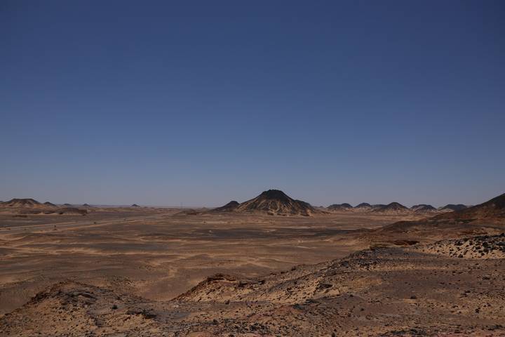 Expansive arid Black Desert landscape with isolated volcanic hill on horizon.