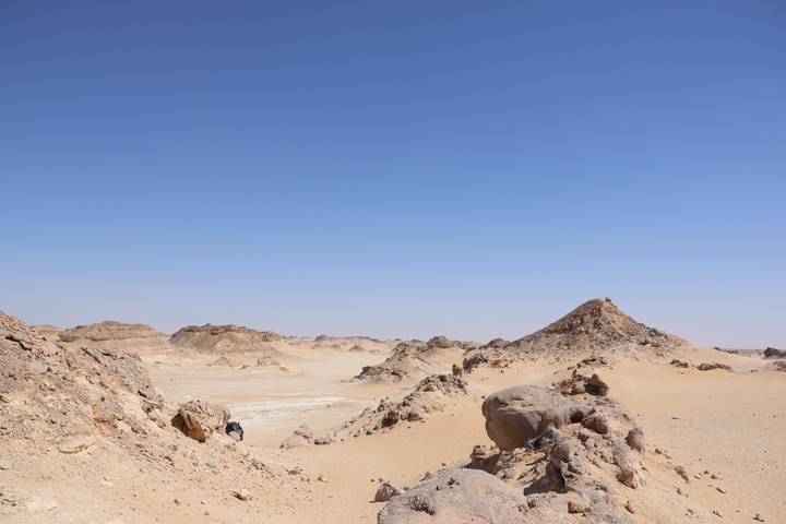 Rocky tan outcrops and sandy valleys under a cloudless blue Egyptian sky.