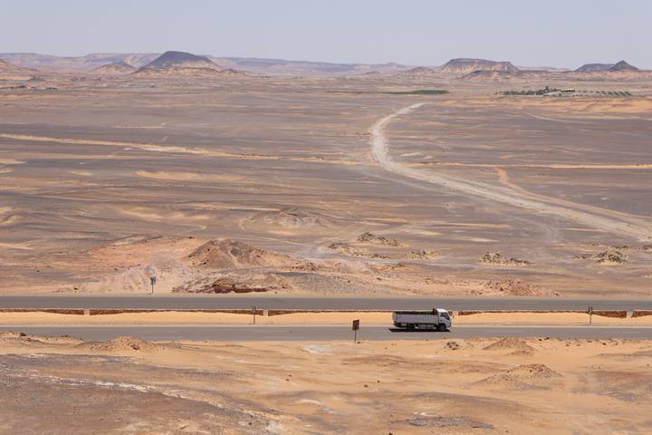 Long desert highway with lone truck winding through barren sandstone plains.