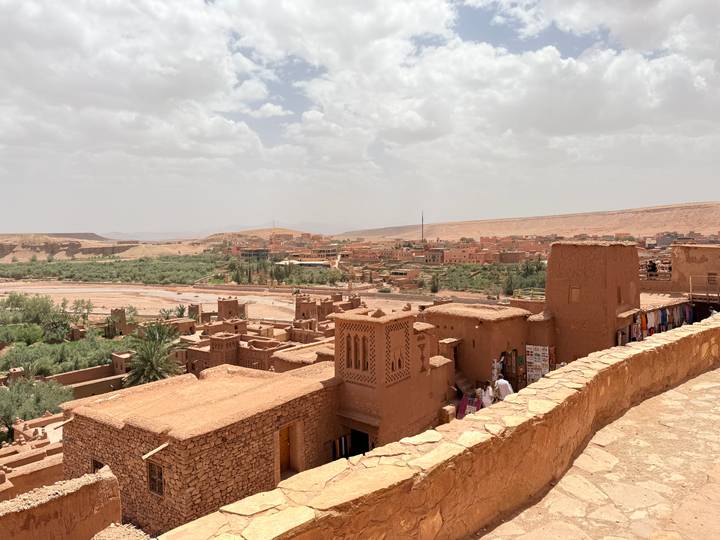 Mud-brick kasbah village overlooking arid valley and oasis patches under hazy sky.
