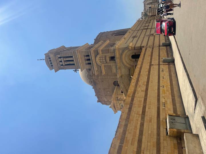 Sand-colored domed church with tall bell tower rising against bright blue Cairo sky.