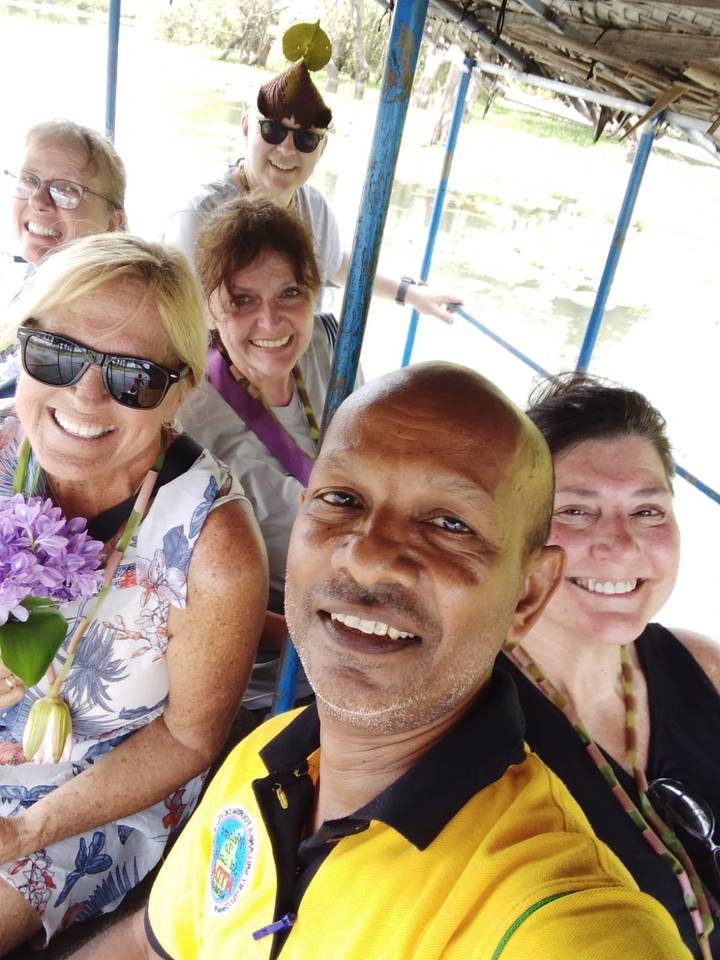 Close selfie of smiling travellers on small open boat with blurred water background.