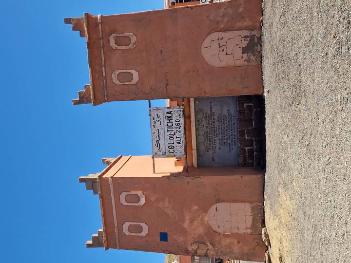 Clay gateway at mountain pass with sign reading "Col du Tichka ALT 2260" against deep blue sky.