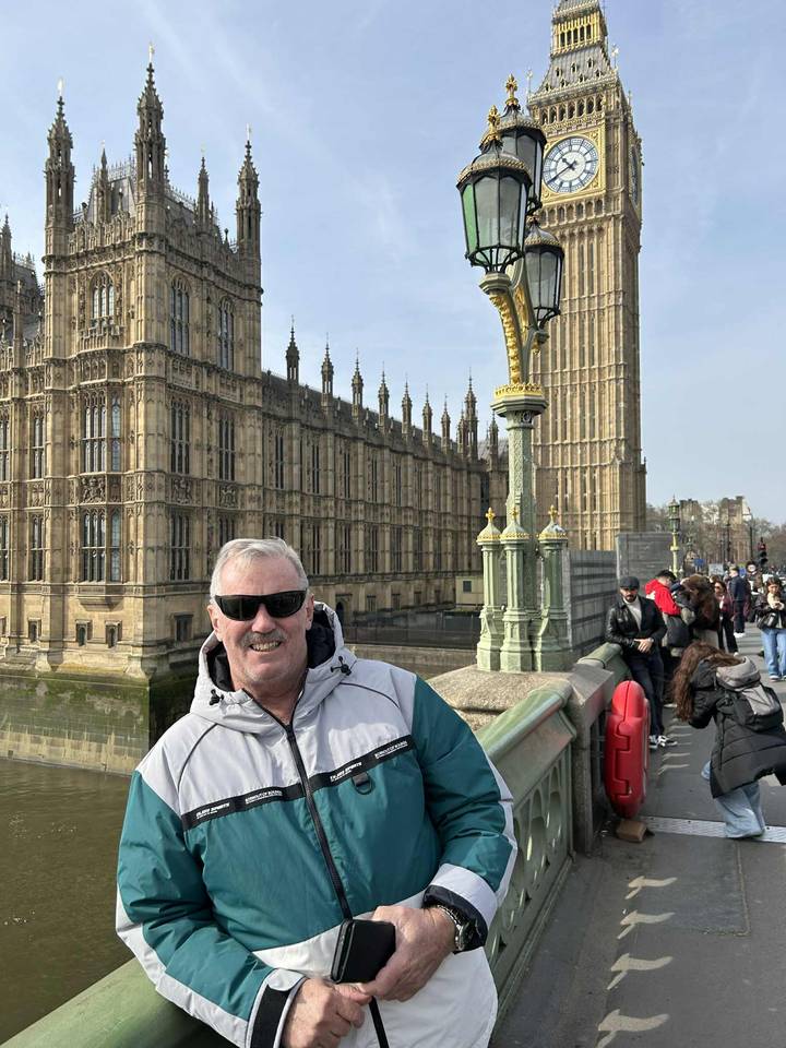 Smiling traveller in sunglasses poses on Westminster Bridge with the neo-Gothic Houses of Parliament towering behind.