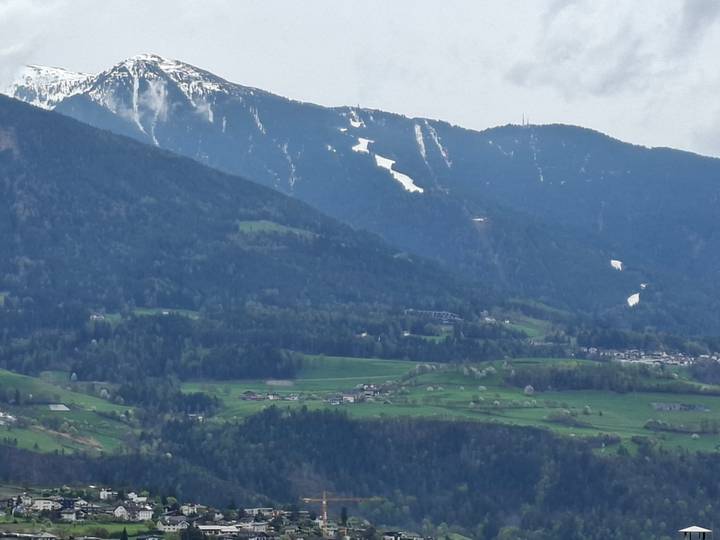 Expansive alpine valley with scattered farms and forested slopes beneath snow-capped mountains.