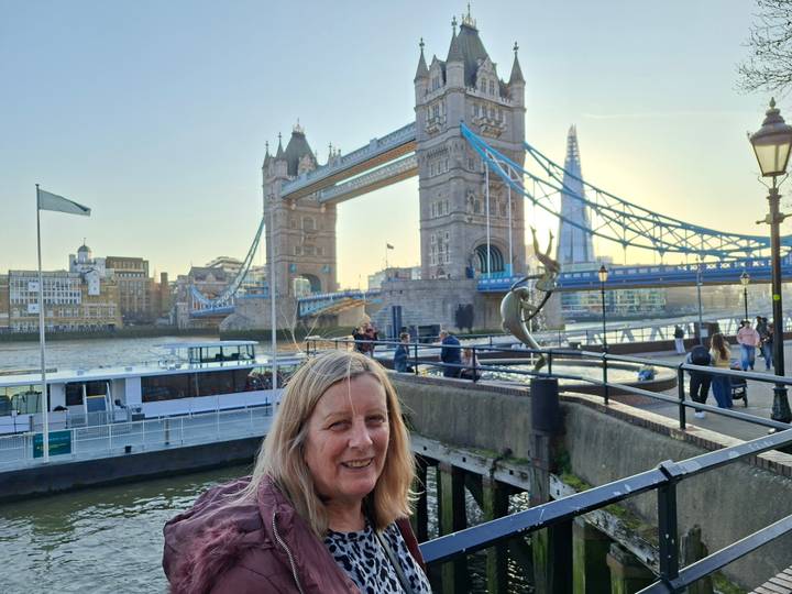 Traveller smiles with Tower Bridge and the Shard in the evening light across the River Thames.