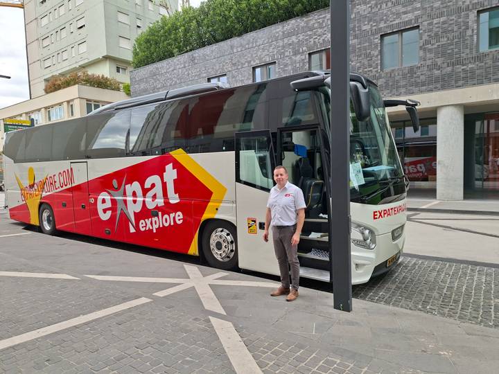 A tour coach with Expat Explore branding parked on a city street while a uniformed driver poses beside it