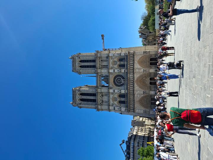 Front view of Notre-Dame Cathedral with many tourists in the plaza under a clear blue sky