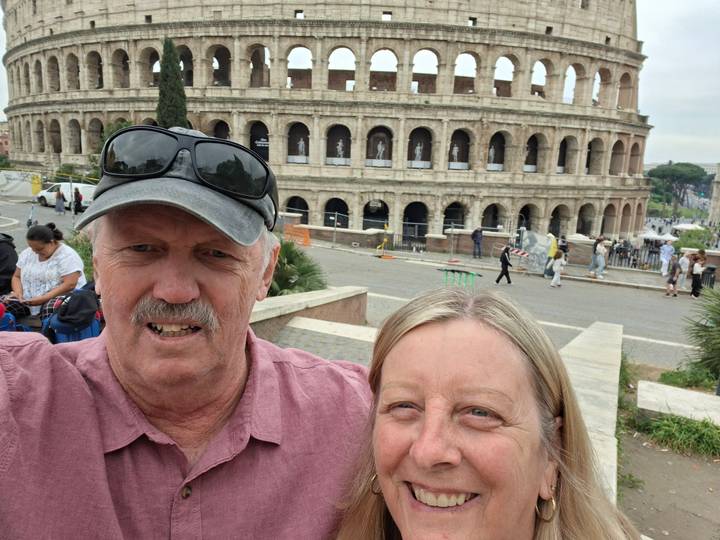 Selfie of a couple with the ancient stone arches of the Colosseum visible behind them